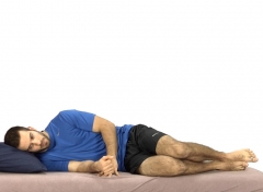 Un homme est allongé sur le côté droit dans un lit, les jambes fléchies, les mains jointes devant lui. Il garde le dos droit, illustrant la position sécuritaire pour sortir ou entrer dans le lit.